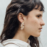Retrato de una mujer con los aretes Hojas de Plátano—variantes pintadas a mano en verde salvia y rust con granulación de vidrio en bronce bañado en oro