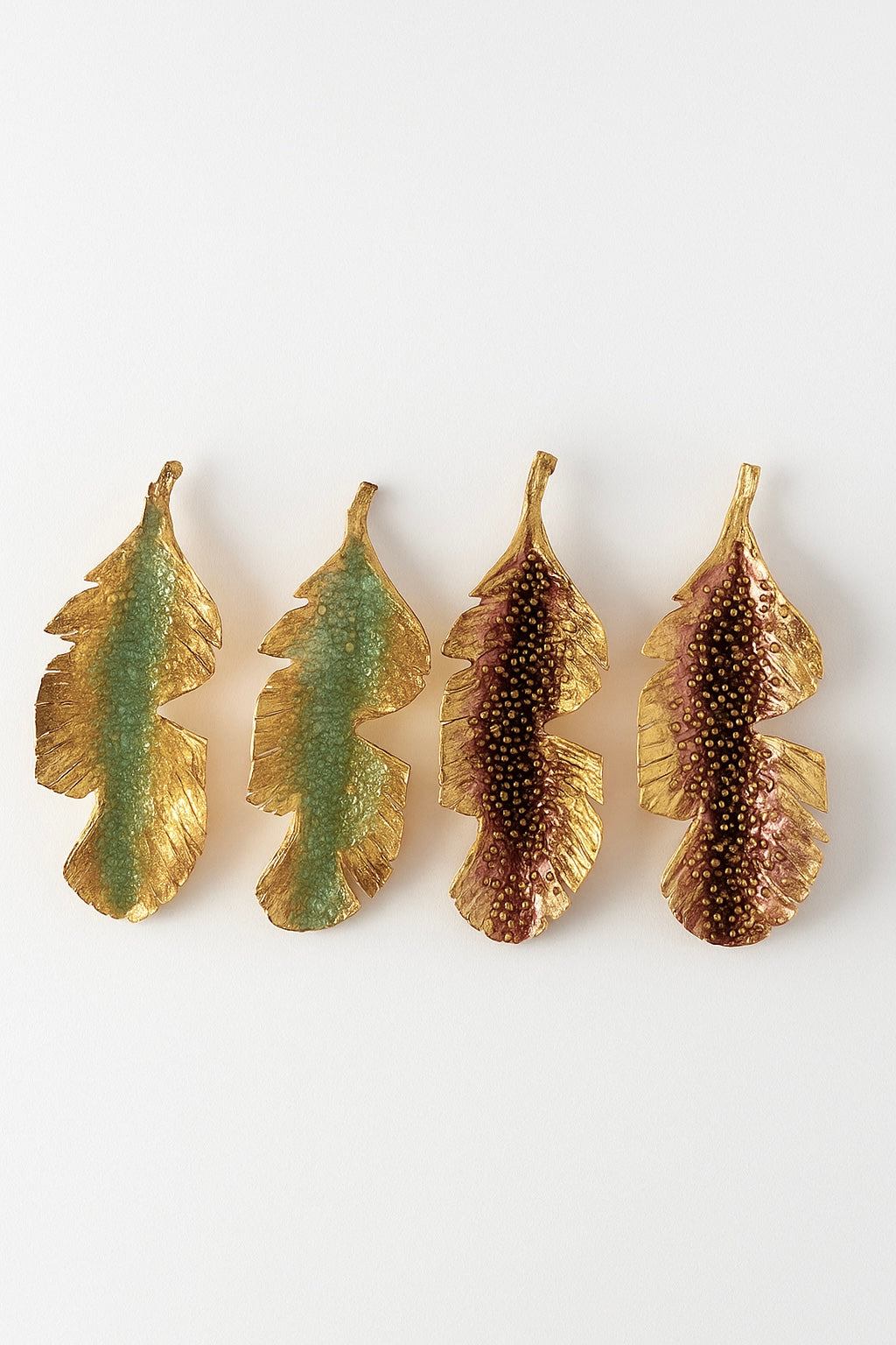 Disposición plana de cuatro aretes Hojas de Plátano alineados horizontalmente sobre fondo blanco—dos pintados a mano en verde salvia y dos en rust—con granulación de vidrio y montura de bronce bañado en oro.