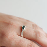 Anillo Refugio de plata esterlina con esmeralda en bruto puesto en una mano, fotografiado sobre fondo neutro claro.