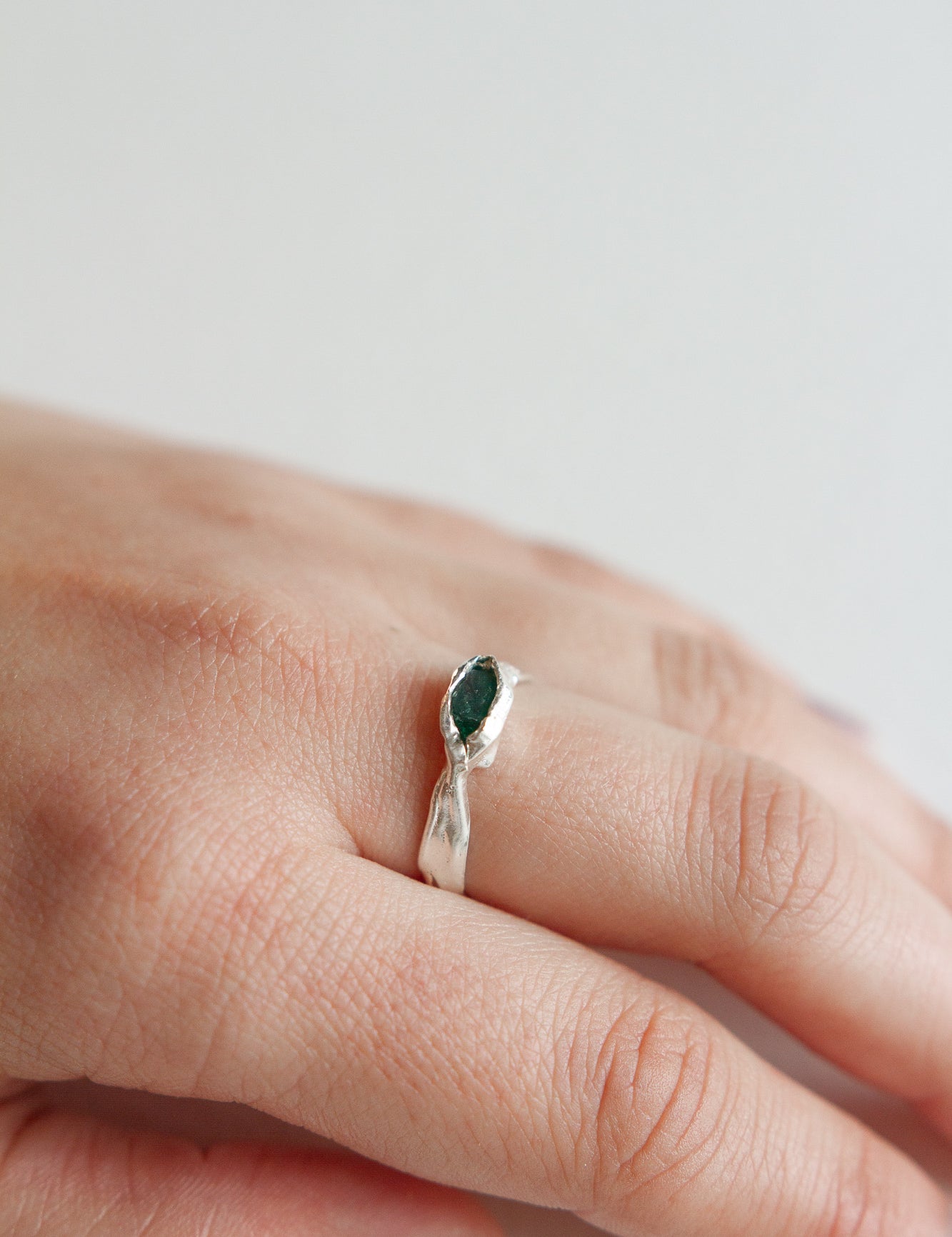 Anillo Refugio de plata esterlina con esmeralda en bruto puesto en una mano, fotografiado sobre fondo neutro claro.
