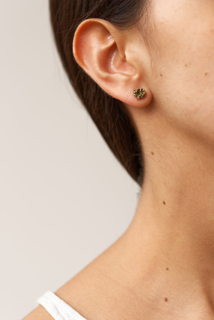 Primer plano lateral de la oreja de una mujer luciendo un arete Topos Coca S, con engaste dorado de volantes relleno de granulación de vidrio y pintura verde.
