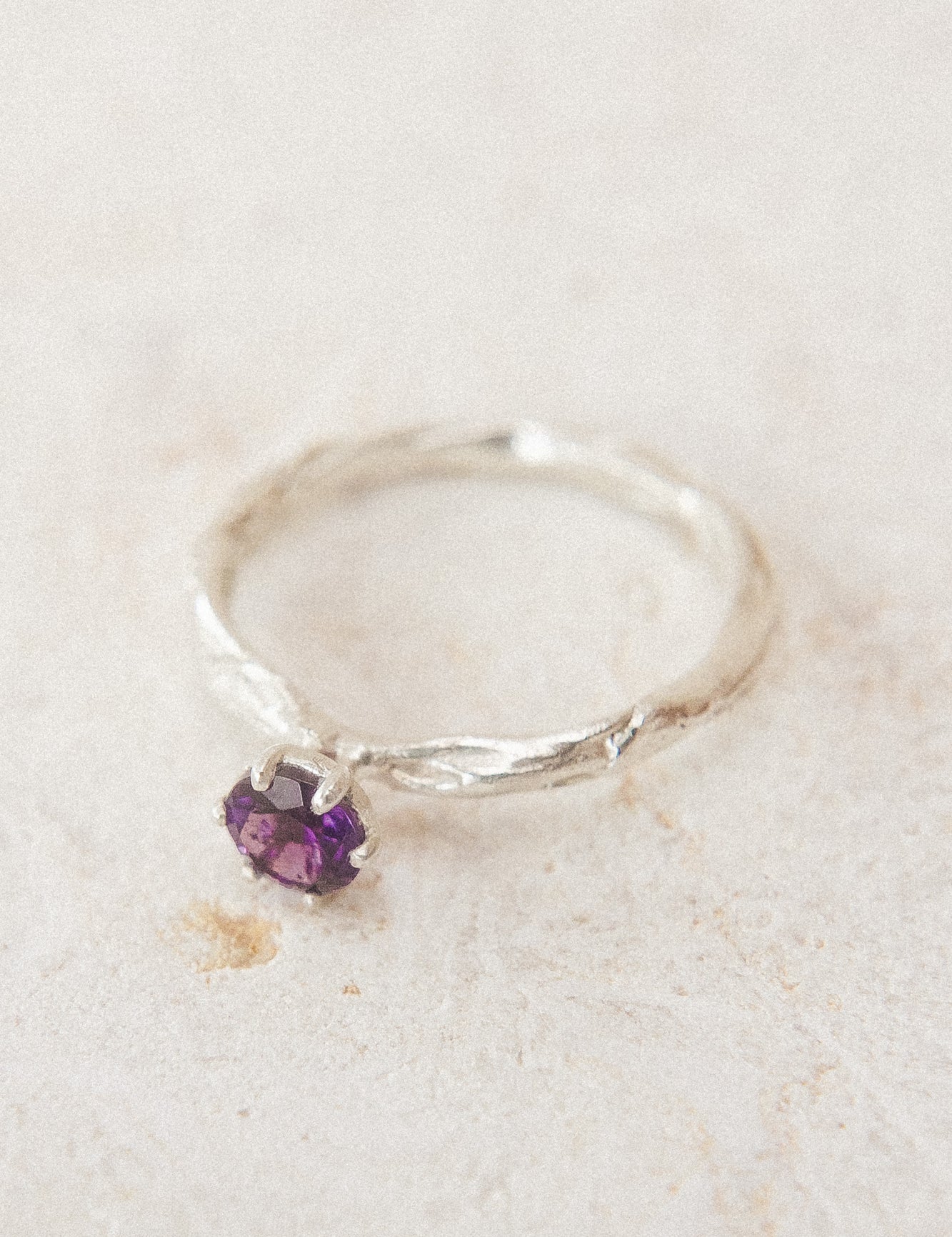 Vista superior del anillo de plata esterlina con una amatista de 4 mm, sobre tela neutra, destacando su textura orgánica y artesanal.