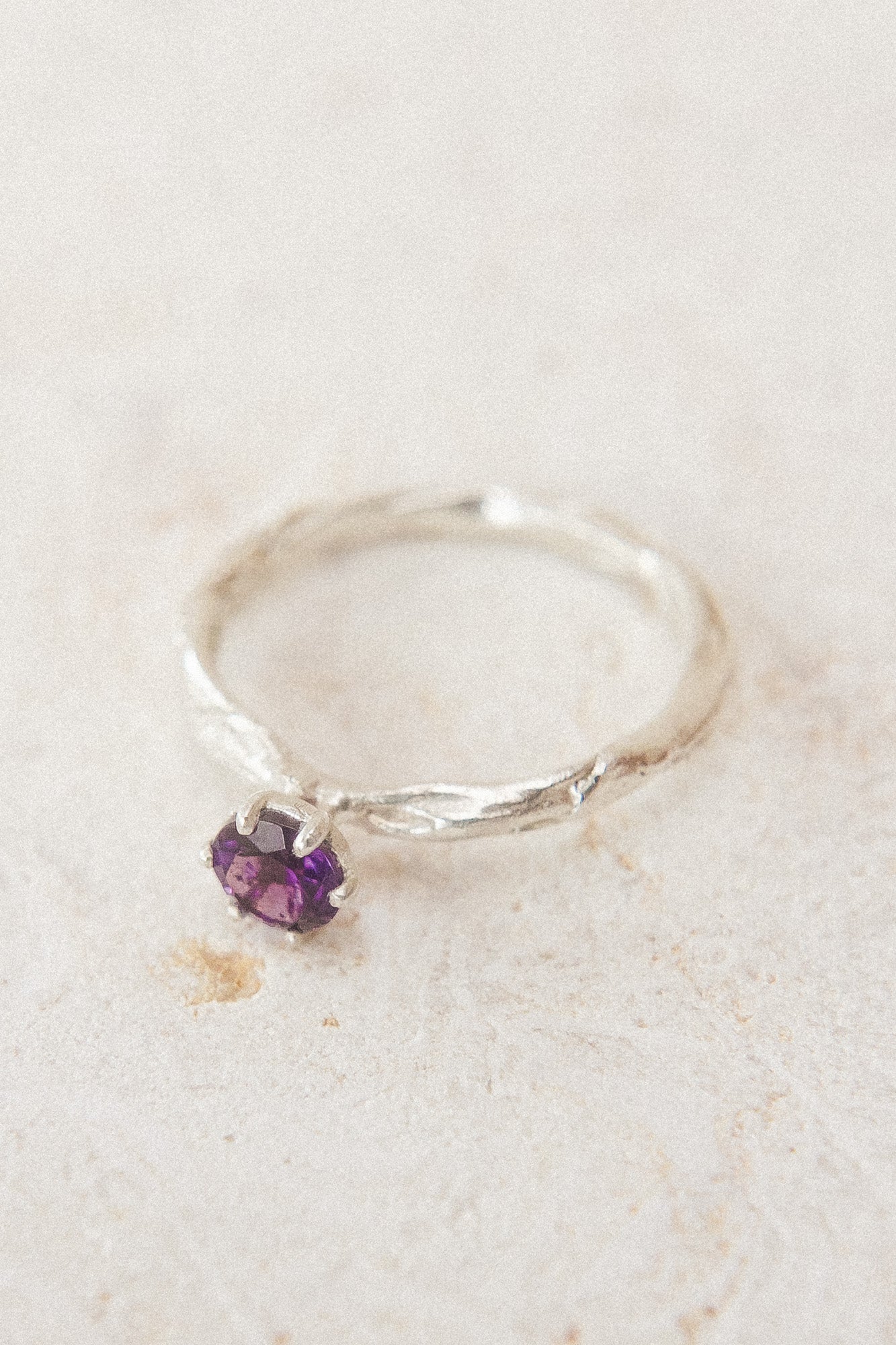 Vista superior del anillo de plata esterlina con una amatista de 4 mm, sobre tela neutra, destacando su textura orgánica y artesanal.