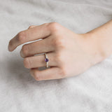 Mano de mujer luciendo el anillo de amatista en plata esterlina, mostrando el ajuste y el perfil delicado de la piedra de 4 mm sobre un fondo suave.