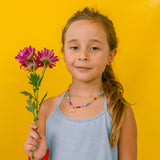 niña con collar arcoíris, sosteniendo  flores sobre fondo amarillo.