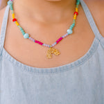 Collar de cuentas multicolor con un colgante dorado en forma de arcoíris, que lleva una niña con un top azul claro.