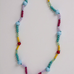 Collar de cuentas de colores con un colgante dorado sobre fondo gris claro.