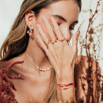 Modelo usando los Aretes Agraz en un ambiente natural con ramas y tonos cálidos.