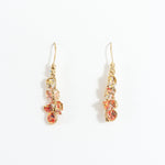 Aretes Azahar en bronce bañado en oro con detalles rojos, diseño botánico y acabado artesanal, sobre fondo blanco.