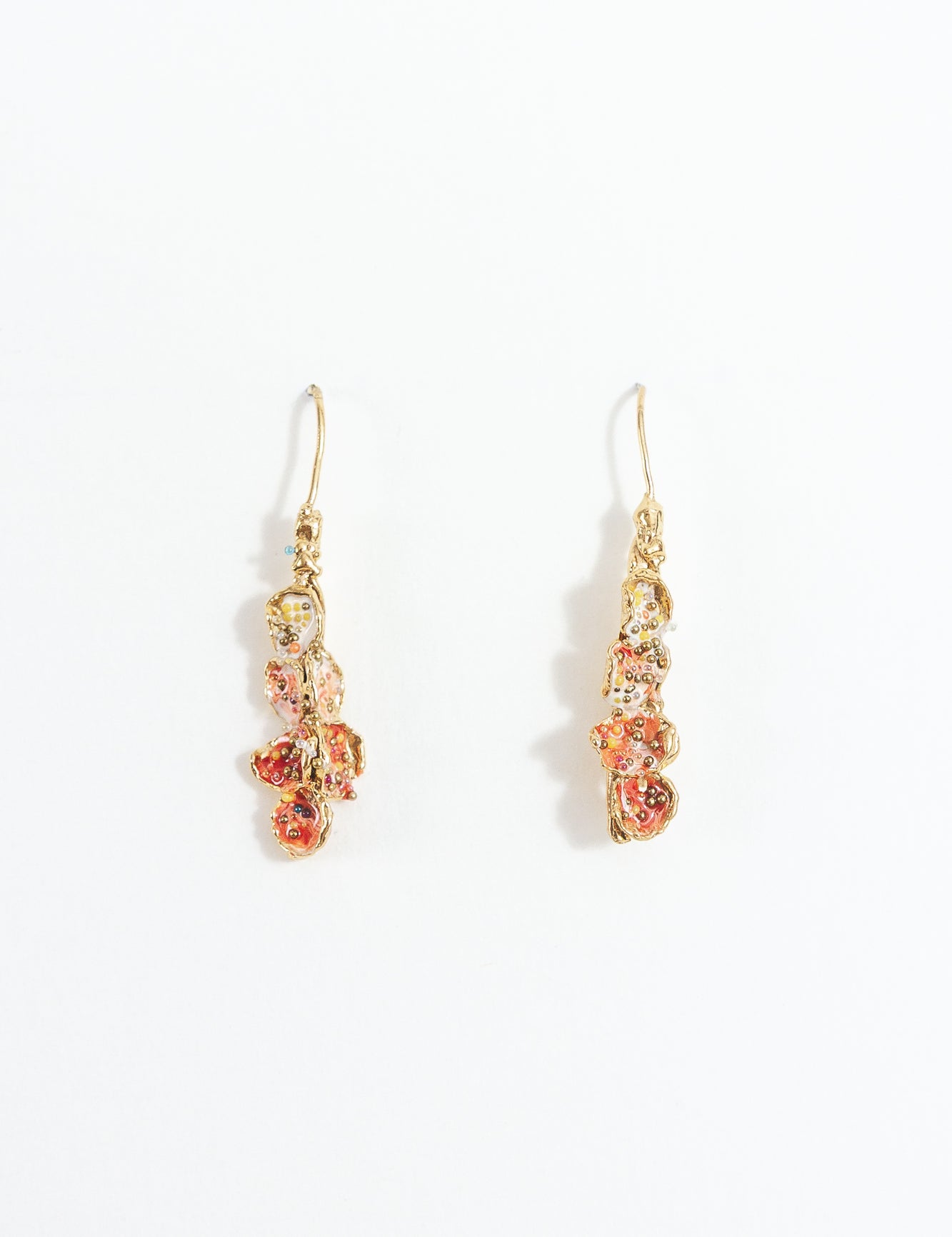 Aretes Azahar en bronce bañado en oro con detalles rojos, diseño botánico y acabado artesanal, sobre fondo blanco.