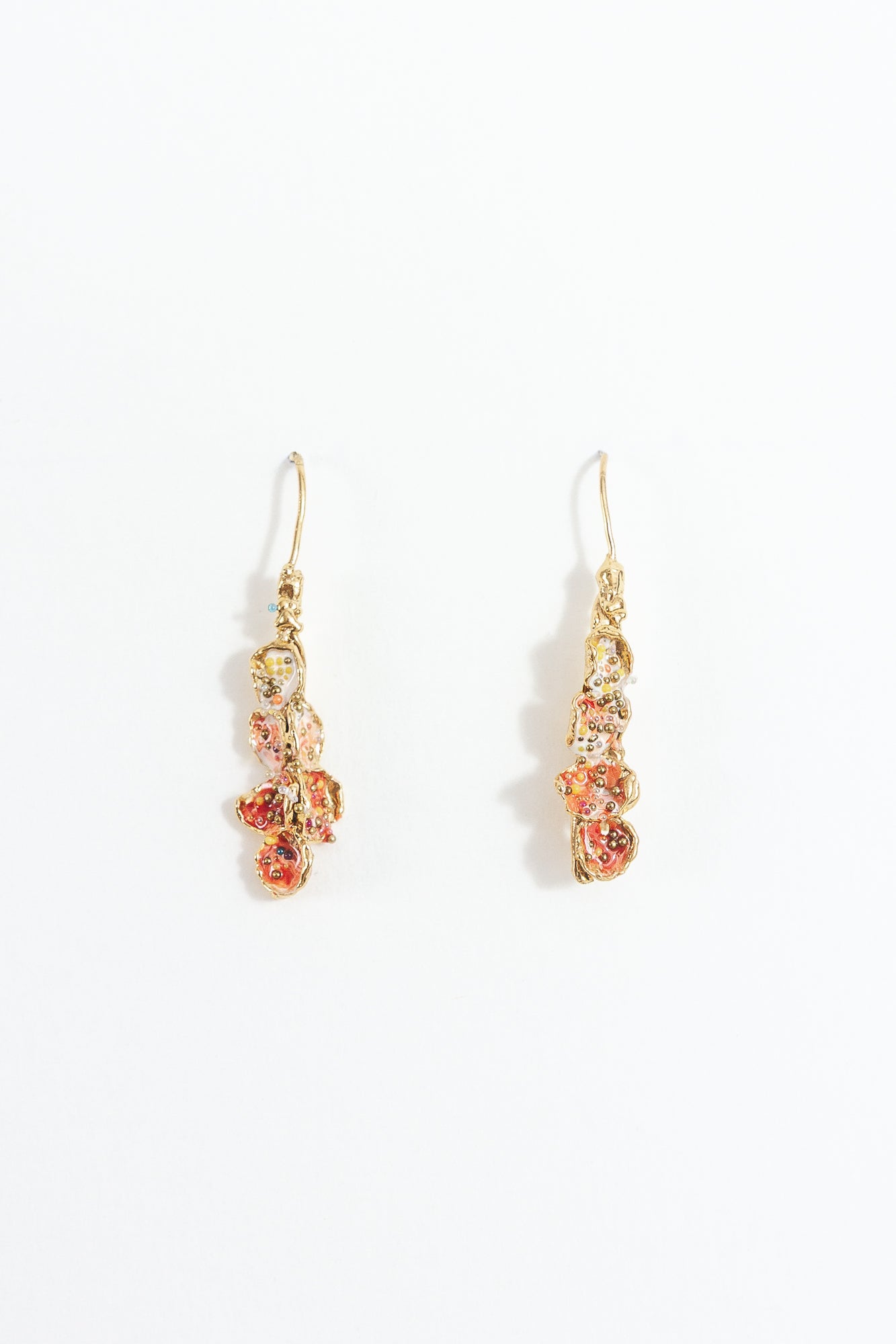 Aretes Azahar en bronce bañado en oro con detalles rojos, diseño botánico y acabado artesanal, sobre fondo blanco.