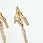 Detalle del diseño superior de los Aretes Raíz, mostrando ramas doradas texturizadas en bronce bañado en oro.