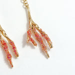 Detalle cercano de los Aretes Raíz en versión roja, con pintura artesanal y granulación de vidrio en tonos coral.