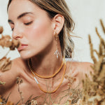 Modelo usando los Aretes Raíz en una composición natural con follaje, resaltando el estilo botánico y artesanal de la joya.