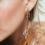 Detalle cercano de los Aretes Raíz llevados por una modelo, en un ambiente natural y cálido que resalta la textura artesanal.