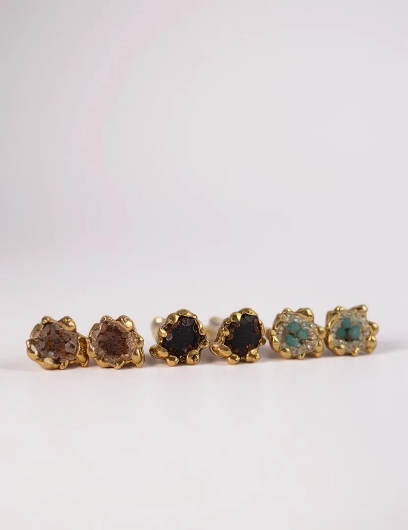 Seis aretes Topos Coca S dispuestos en línea horizontal sobre fondo claro, cada uno con engaste dorado de volantes relleno de granulación de vidrio y pintura en tonos marrón, negro, verde, turquesa y más.