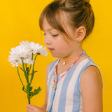 niña con vestido azul claro usando el Collar Margarita artesanal con dije dorado y cadena de cristales rosa.