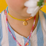 Primer plano de niña usando el Collar Margarita con dije dorado pintado a mano y cadena de hilo con cristales.