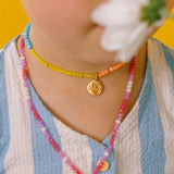 Primer plano de niña usando el Collar Margarita con dije dorado pintado a mano y cadena de hilo con cristales.