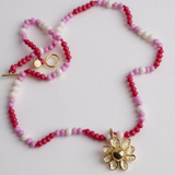 Collar Margarita artesanal con dije dorado en forma de flor, dispuesto en círculo sobre fondo blanco.