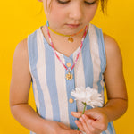 Niña con vestido azul mirando hacia abajo mientras luce el Collar Margarita artesanal con dije dorado.