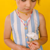 Niña con vestido azul mirando hacia abajo mientras luce el Collar Margarita artesanal con dije dorado.