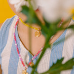 Detalle del dije dorado del Collar Margarita rodeado de cristales rosa, blanco y fucsia.