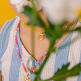 Detalle del dije dorado del Collar Margarita rodeado de cristales rosa, blanco y fucsia.