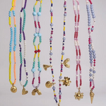 Conjunto de collares de cuentas de colores con varios colgantes sobre un fondo gris claro.