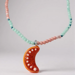 Collar Naranja enrollado sobre fondo blanco, mostrando varias vueltas de cuentas en verde menta y rosa con el colgante de media luna naranja visible.