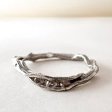Anillo artesanal de plata con diamantes de laboratorio, diseño orgánico en forma de rama, colocado sobre una superficie blanca.