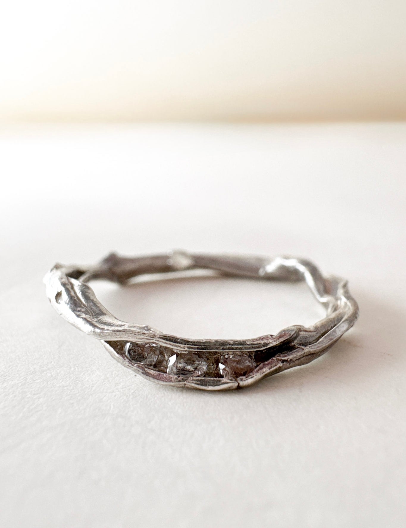 Anillo artesanal de plata con diamantes de laboratorio, diseño orgánico en forma de rama, colocado sobre una superficie blanca.