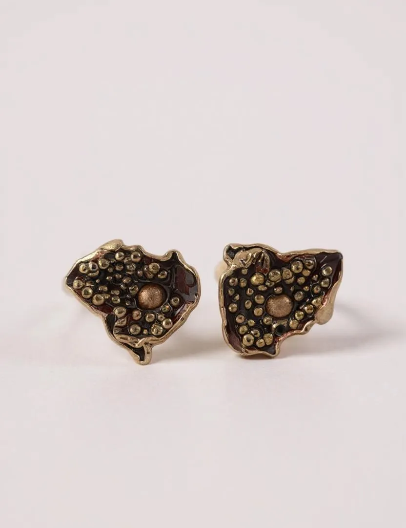 Par de aretes Topos Cucu en bronce bañado en oro, pintados a mano en color rust con granulación de vidrio, sobre fondo rosa pálido.