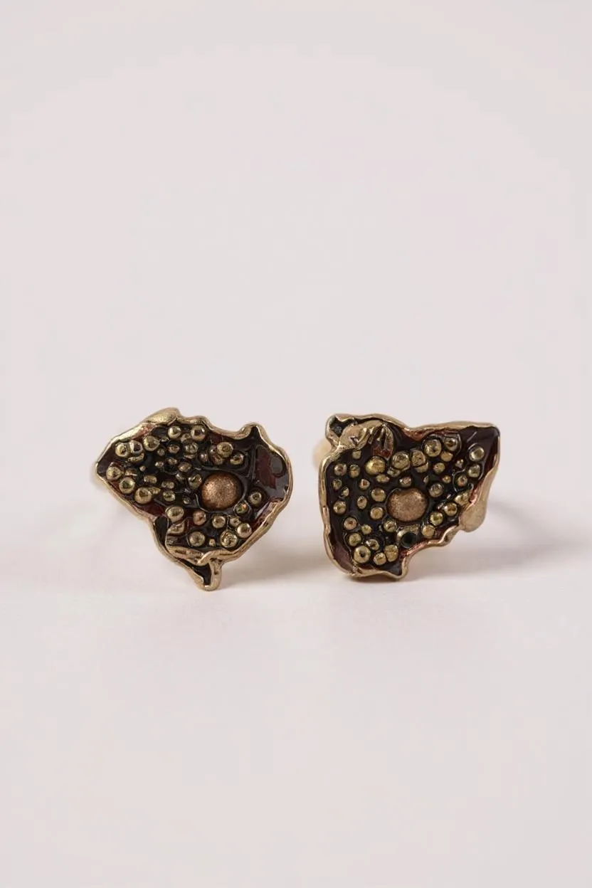 Par de aretes Topos Cucu en bronce bañado en oro, pintados a mano en color rust con granulación de vidrio, sobre fondo rosa pálido.