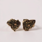 Par de aretes Topos Cucu en bronce bañado en oro, pintados a mano en color rust con granulación de vidrio, sobre fondo rosa pálido.