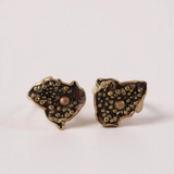 Par de aretes Topos Cucu en bronce bañado en oro, pintados a mano en color rust con granulación de vidrio, sobre fondo rosa pálido.