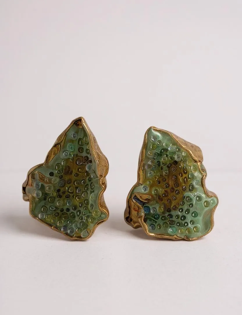 Disposición plana de dos aretes Topos Cucu en bronce bañado en oro, pintados a mano en verde salvia con granulación de vidrio, sobre fondo blanco.