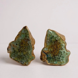 Disposición plana de dos aretes Topos Cucu en bronce bañado en oro, pintados a mano en verde salvia con granulación de vidrio, sobre fondo blanco.