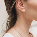 Primer plano lateral de la oreja de una mujer con el cabello recogido detrás, luciendo un arete topos de estrella bañados en oro.