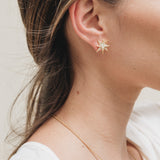 Primer plano lateral de la oreja de una mujer con el cabello recogido detrás, luciendo un arete topos de estrella bañados en oro.