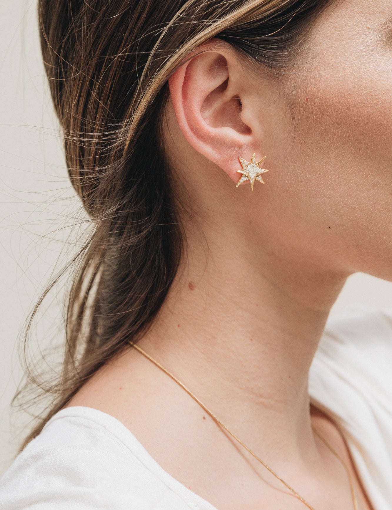 Primer plano lateral de la oreja de una mujer con el cabello recogido detrás, luciendo un arete topos de estrella bañados en oro.