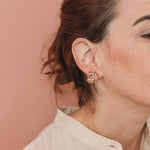  Perfil de una mujer luciendo un arete Galaxea en color Rust, bañado en oro con gránulos de vidrio, cabello recogido, sobre un fondo terracota suave.