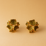 Dos aretes Galaxea en color sage: bañados en oro, con forma floral y gránulos de vidrio verde salvia, colocados lado a lado sobre un fondo beige cálido.