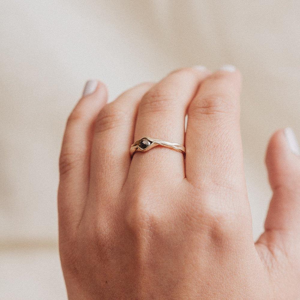 Anillo de oro amarillo 10k con diamante sal y pimienta puesto en una mano, fotografiado sobre fondo de tela beige suave.