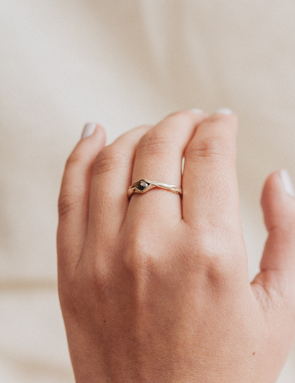 Anillo de oro amarillo 10k con diamante sal y pimienta puesto en una mano, fotografiado sobre fondo de tela beige suave.