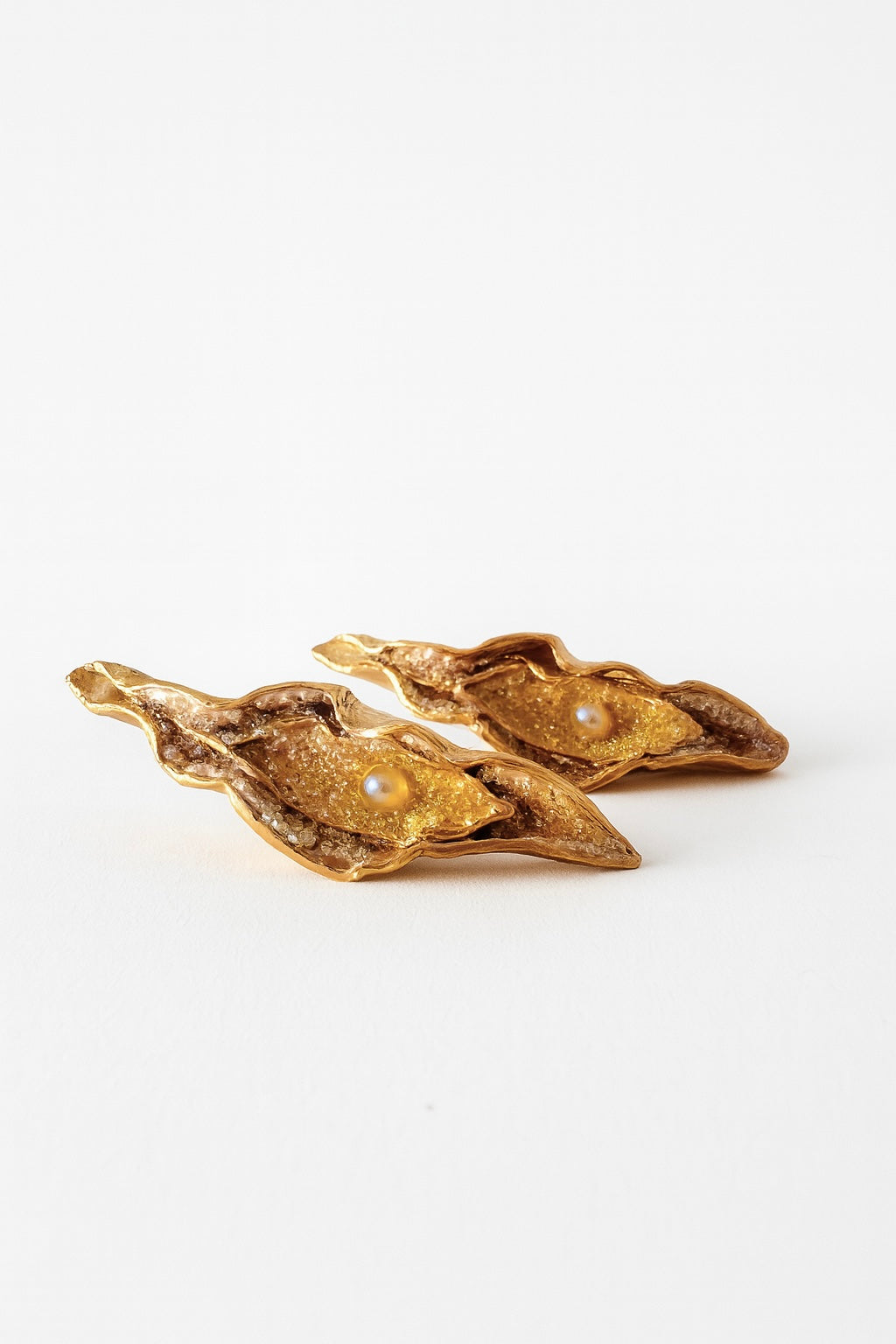 Disposición plana de dos Aretes Lechuga variante Mustard en bronce bañado en oro, pintados a mano en rust con granulación de vidrio, sobre fondo blanco.