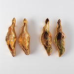 Disposición plana de cuatro Aretes Lechuga sobre fondo blanco—dos pintados a mano en amarillo mostaza y dos en rust, todos con granulación de vidrio y montura de bronce bañado en oro.