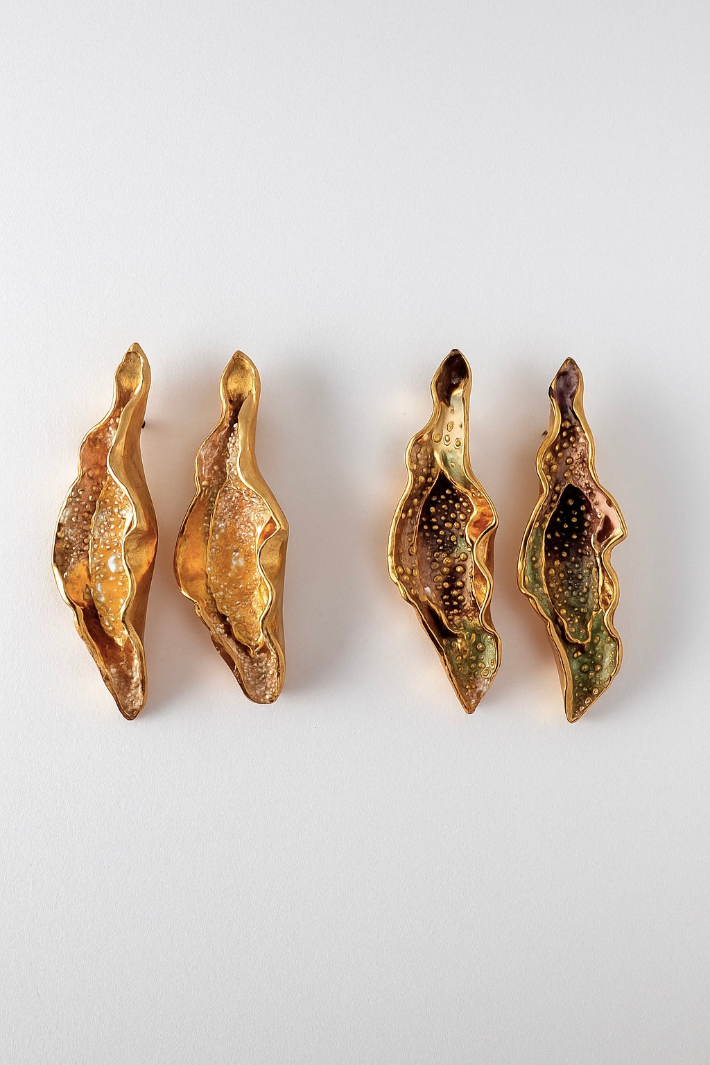Disposición plana de cuatro Aretes Lechuga sobre fondo blanco—dos pintados a mano en amarillo mostaza y dos en rust, todos con granulación de vidrio y montura de bronce bañado en oro.