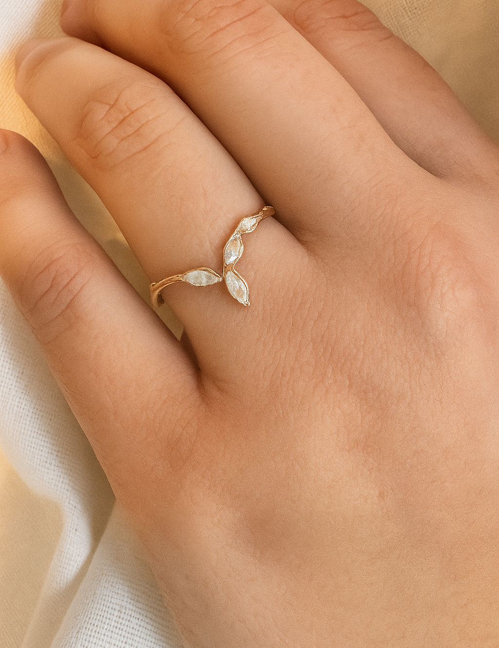 Anillo Marqueza en oro rosado con circones puesto en una mano, fotografiado sobre tela suave.