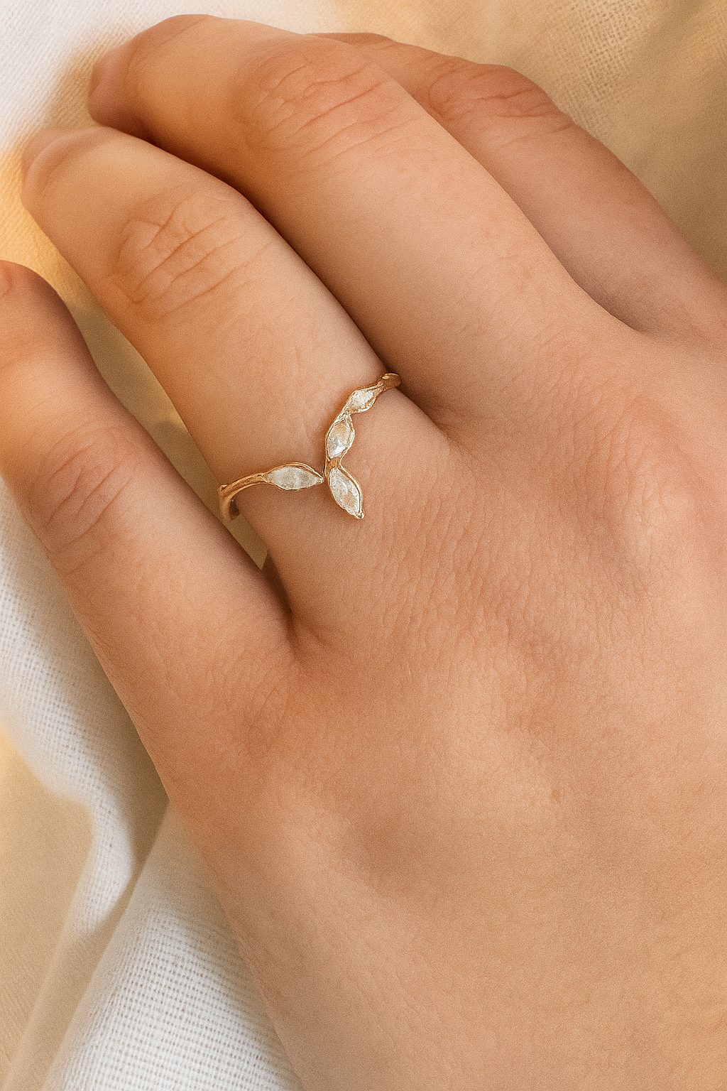 Anillo Marqueza en oro rosado con circones puesto en una mano, fotografiado sobre tela suave.